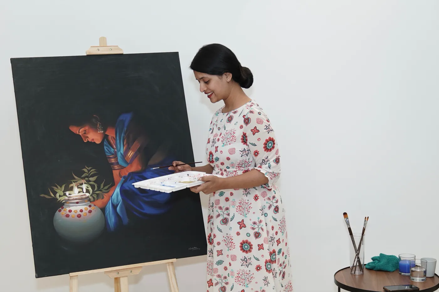 Naishitha standing beside her painting of a woman lighting a lamp
